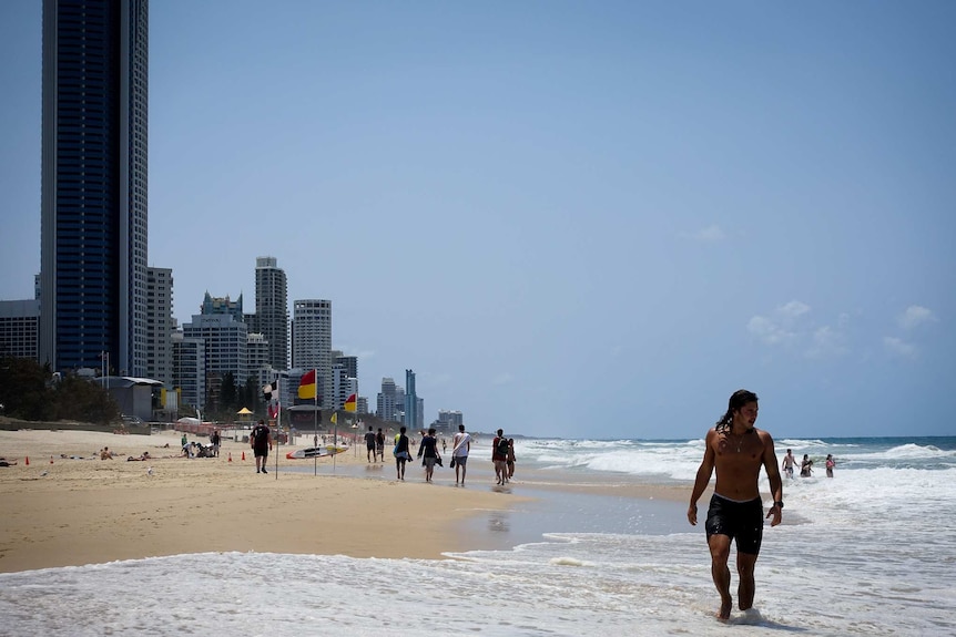 A man walks along a long stretch of city beach.