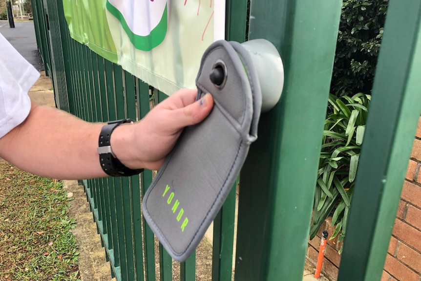 A hand holds a pouch which is attached to a fence and has the name YONDR on it.