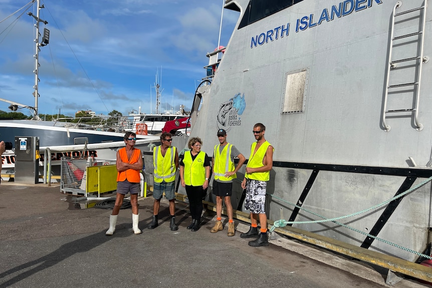 Photo of a group of men and women standing in front of a boat.