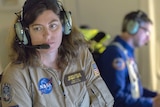 A woman wearing a NASA jumpsuit and headset.