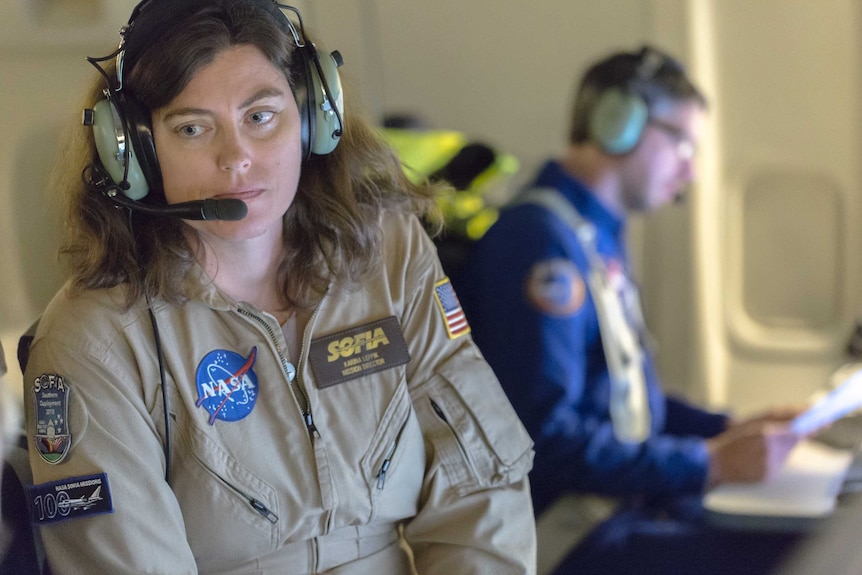 A woman wearing a NASA jumpsuit and headset.