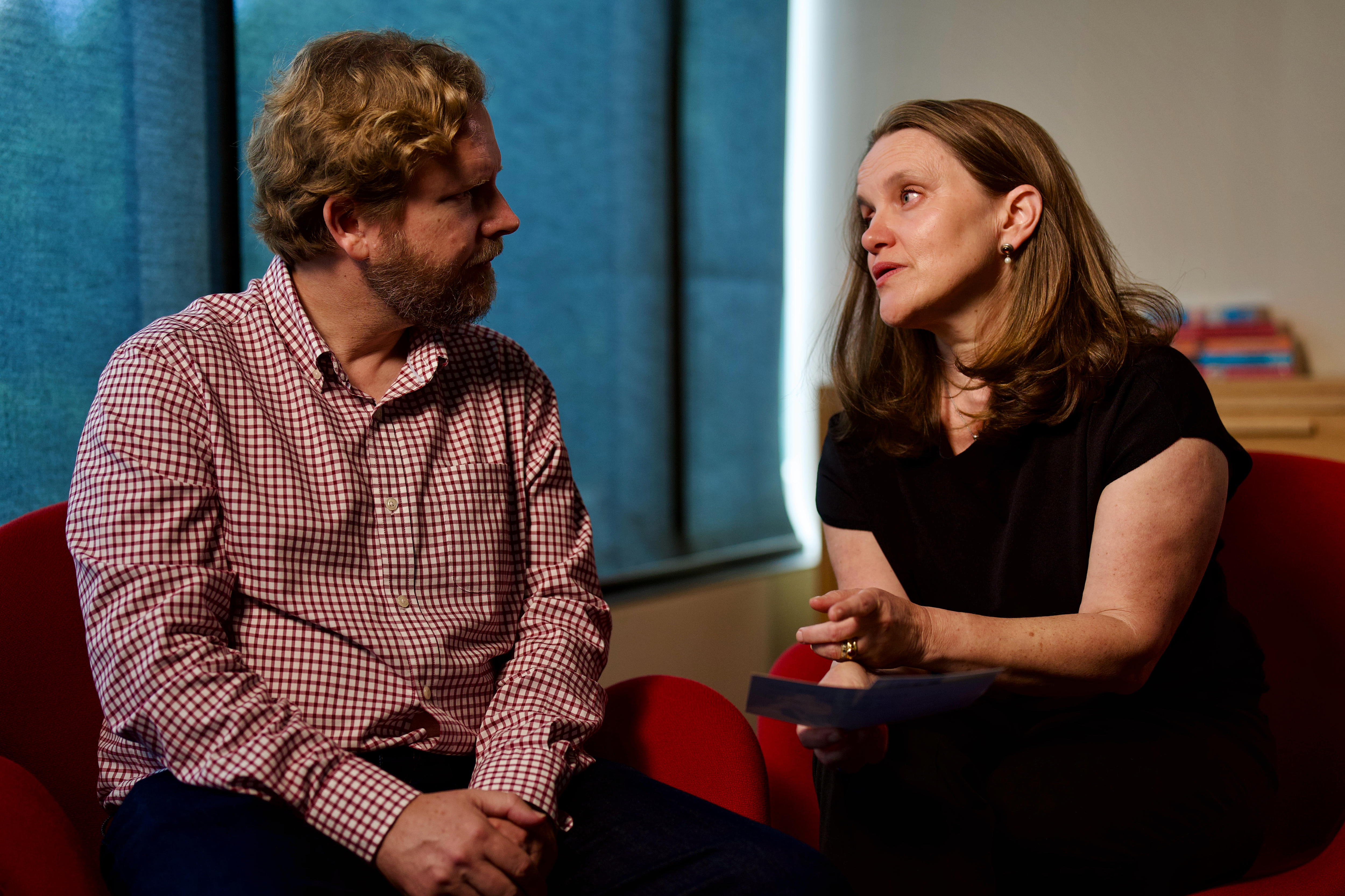 Una mujer con un top negro habla con un hombre con una camisa roja y blanca.
