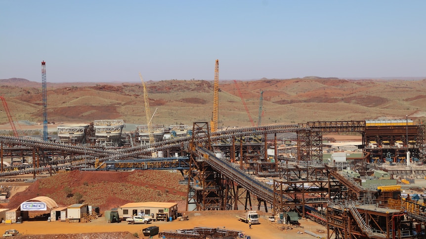 A photo of lots a giant equipment plant in the Pilbara, red dirt in front and behind it, blue sky above it.