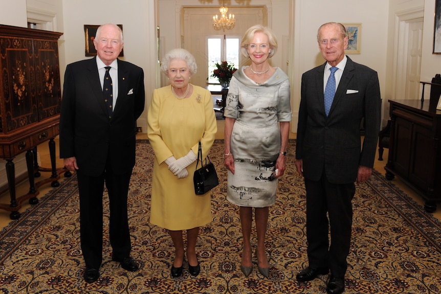 Michael Bryce, the Queen, Quentin Bryce and Prince Phillip pose and smile in a line in a sitting room