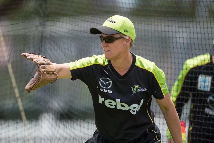 Jo Broadbent holds a baseball glove out to take a catch wearing green and black kit