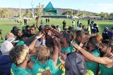 A team of Indigenous football players gather to congratulate each other at the end of a game.