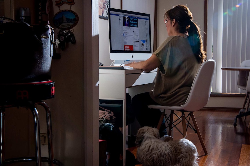 Sandy sits at a computer. A dog stands at her feet.