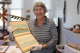 A woman holding a sketchbook with watercolour drawings in it stands at a musuem.