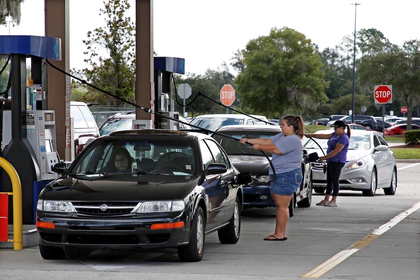 People fill their cars at the bowser as vehicles queue up behind them