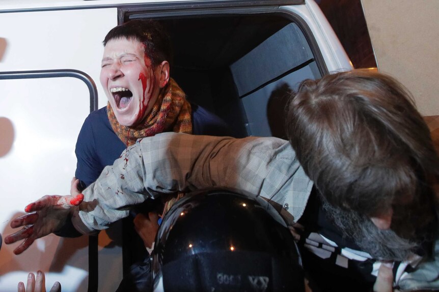 Riot police officers detain a protester in St Petersburg. The protester has blood on their head and their hands.