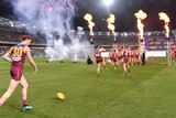 Brisbane Lions players run on to the field as fireworks, flame and smoke surround their entrance