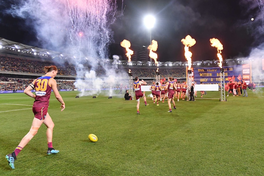 Brisbane Lions players run on to the field as fireworks, flame and smoke surround their entrance