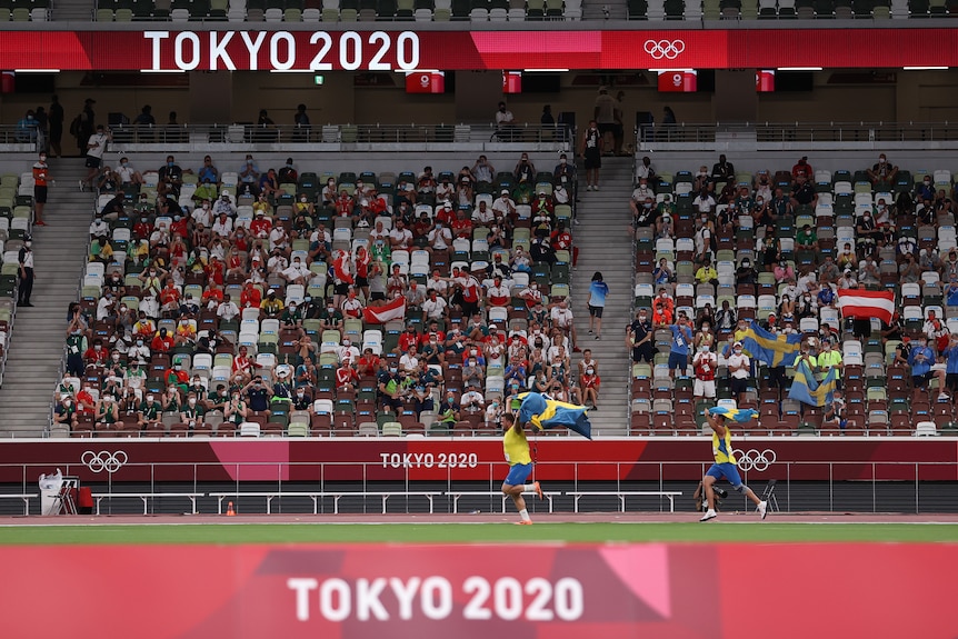 Two athletes running in front of a stadium crowd while holding their country's national flag in the air 