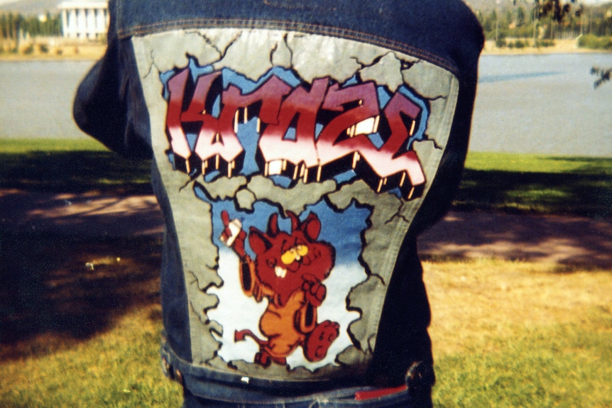 A boy wears a denim jacket painted with graffiti on its back