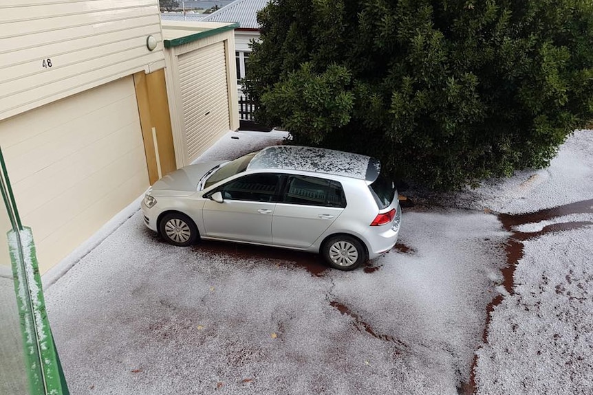 A car sits in front of an iced garage with sleet on the ground, next to a green tree.