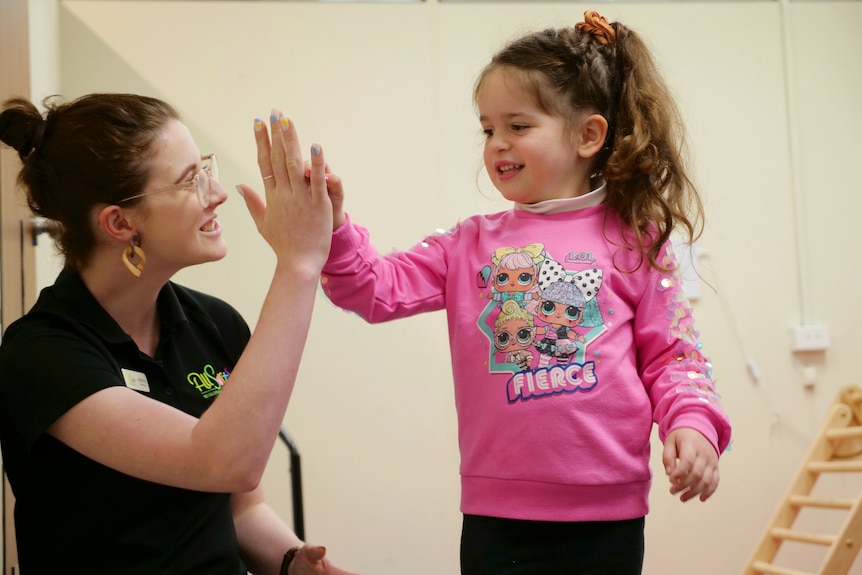 Arlo in a pink jumper, smiling, giving her Johanna a high five.