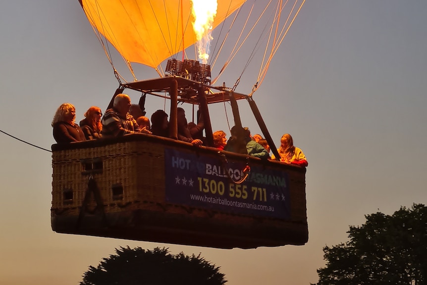 A hot air balloon basket rises into a pre-dawn morning. 