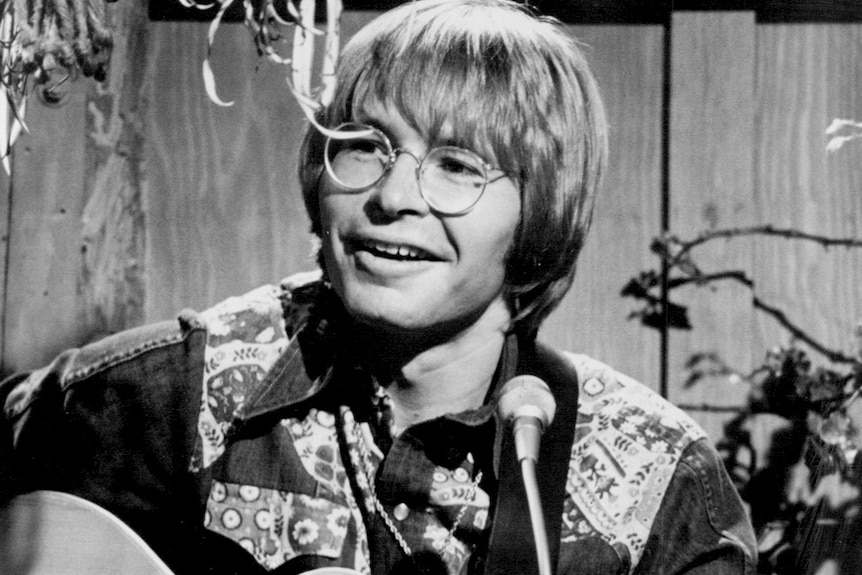Black and white photo of John Denver singing and playing guitar.