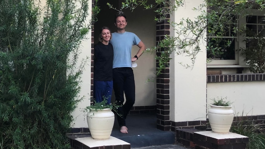 A young couple stand on the porch of a brick home