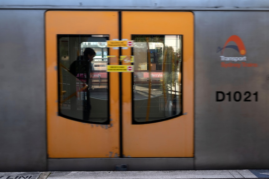 A Sydney train begins to move at a station. Through the glass on the doors the silhouette of a person can be seen.