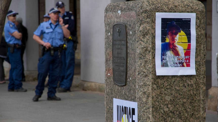 Police gather in the background, behind photos of Elijah Doughty hung outside the Kalgoorlie courthouse during the trial.