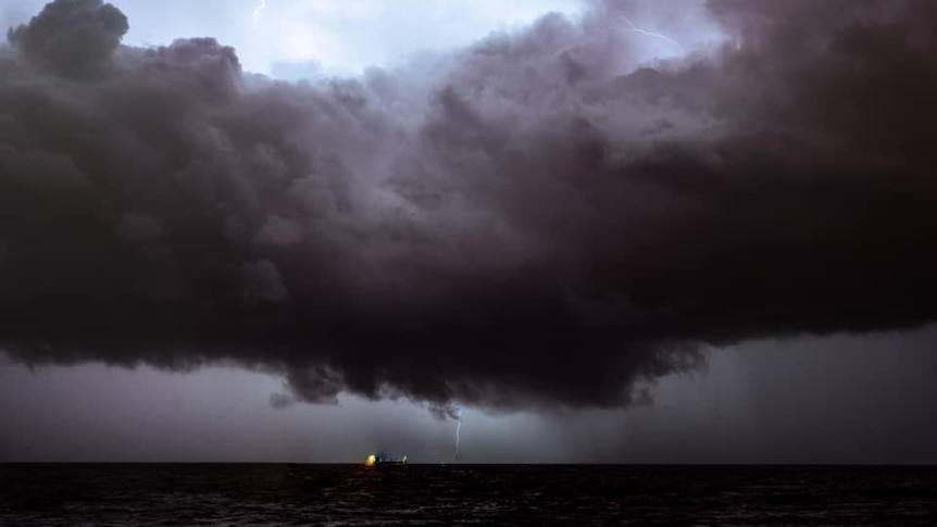 Nubes de tormenta oscuras y relámpagos en la distancia hacia el mar frente a la playa de Trigg.
