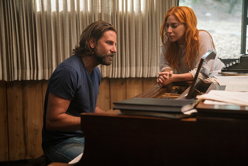 Colour still of Lady Gaga watches Bradley Cooper plays piano in rehearsal room in 2018 film A Star is Born.
