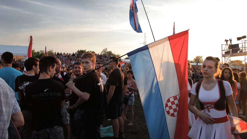 A crowd of young adults in traditional dress hold the Croatian flag.