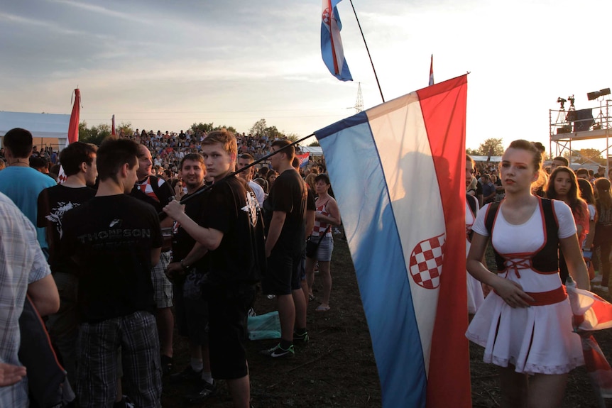 A crowd of young adults in traditional dress hold the Croatian flag.