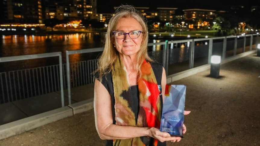 A photo of a woman with blonde hair holding an award at the Darwin waterfront at night.
