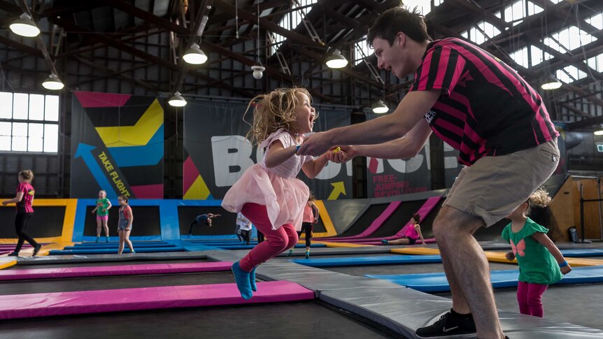 Young girl with blonde hair bounces on a trampoline with a staff member at Bounce