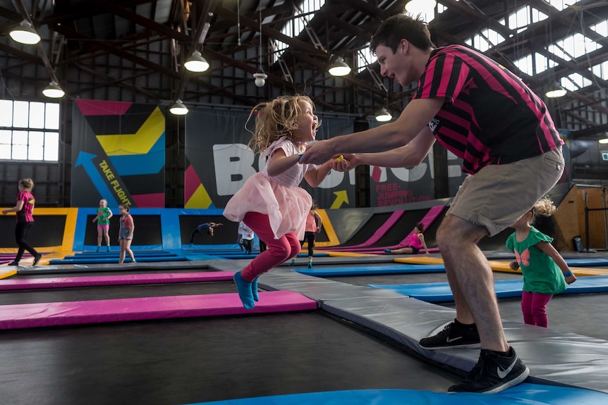 Young girl with blonde hair bounces on a trampoline with a staff member at Bounce