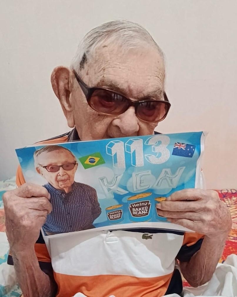 A man who is 114 holds up a birthday card for Ken Weeks who is 113