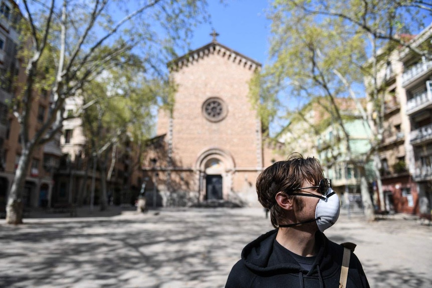 Andrew Burden wearing a face mask, stands in the deserted plaza outside his home in Spain.
