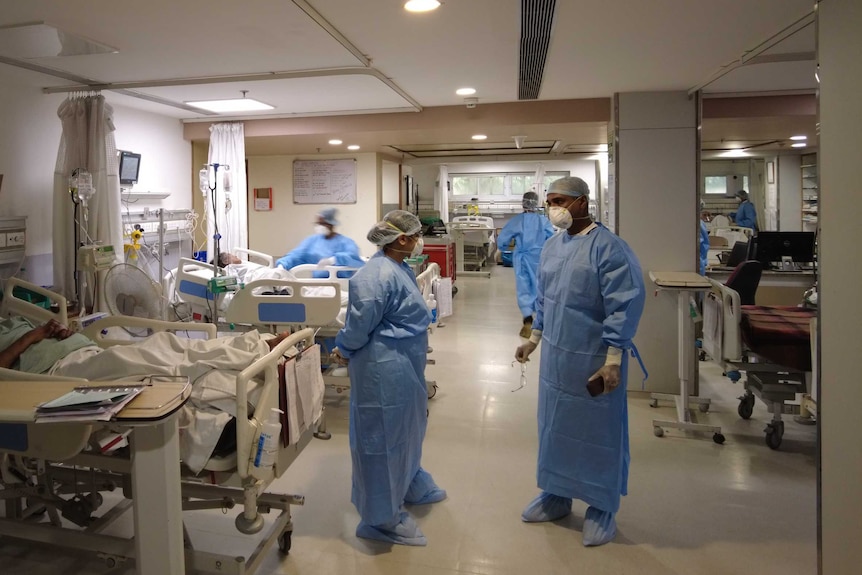 Two health workers in scrubs and masks talk on a ward