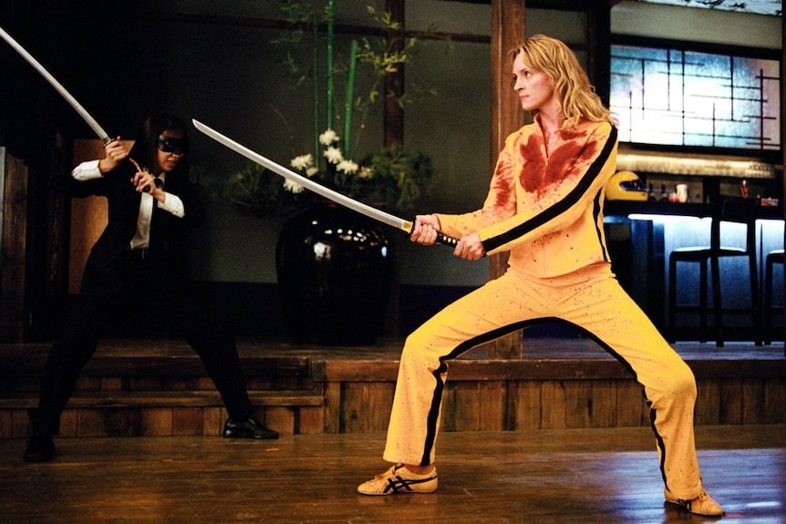 电影《杀死比尔》剧照：一名女性穿着黄色套装和球鞋，手持一把武士刀。
