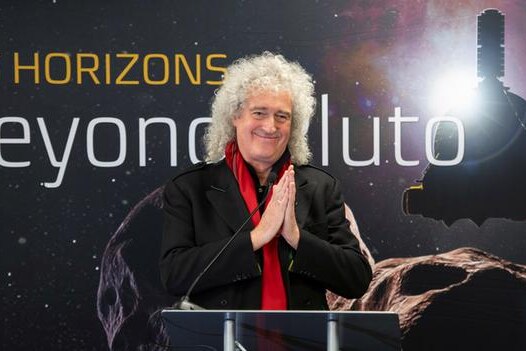 Brian May smiles with his hands pressed together