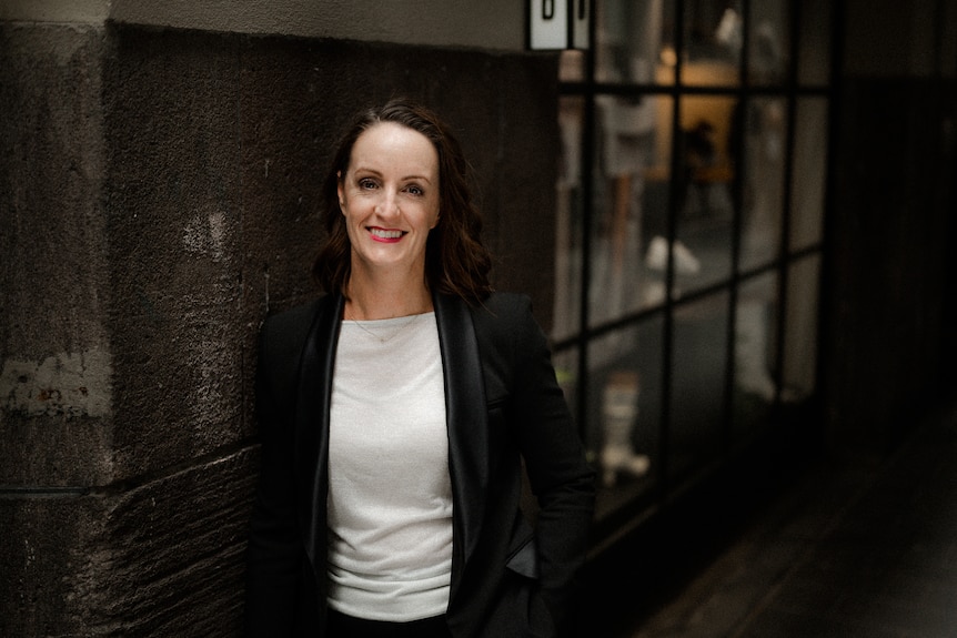 A woman in a black suit stares into the camera.