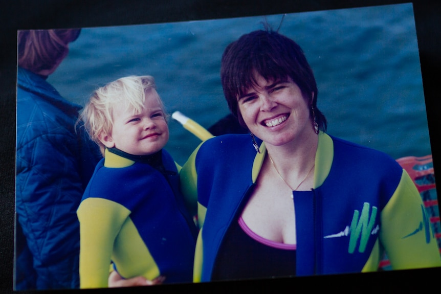 A photo of a mum holding a blonde baby on a boat