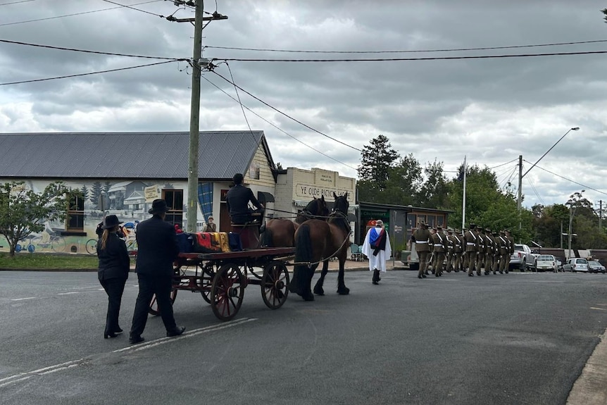 Funeral procession with horse drawn cart walks down country street.