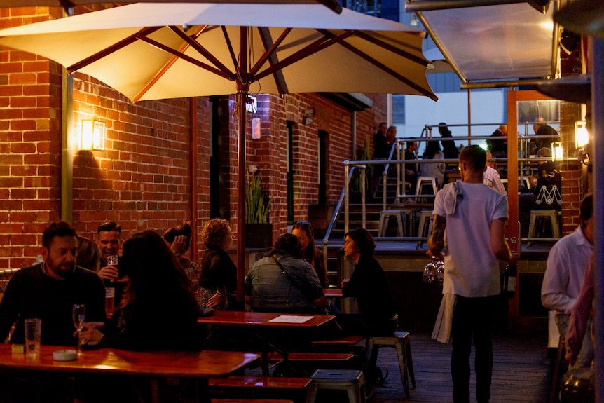 A busy urban bar outdoor area with tables, umbrellas, exposed red brick walls and warm lighting at dusk.