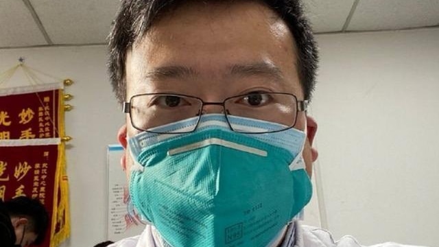 A man with a medical mask and glasses takes a selfie. He has short dark hair.