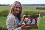 A lady holds up a Mother's Day hamper in a vineyard.