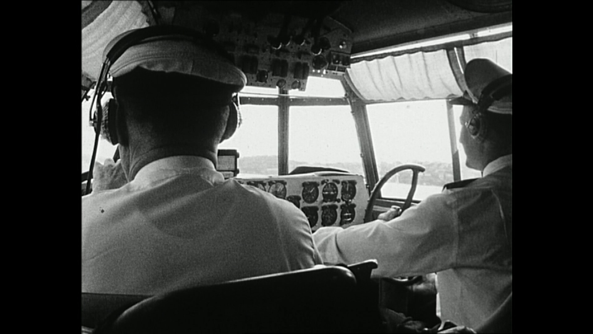 Two pilots inside an old flying boat in an archival black and white photo.