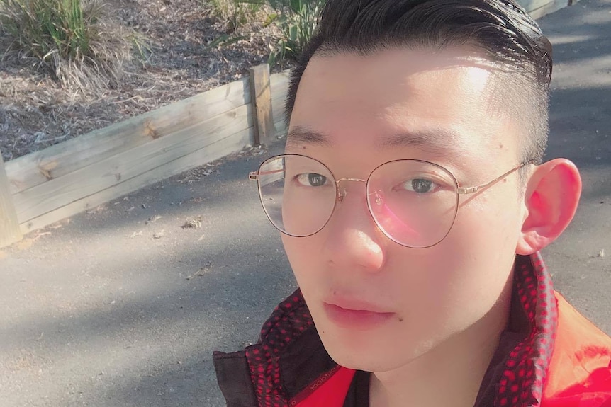 A man with black hair and glasses taking a close up selfie photo