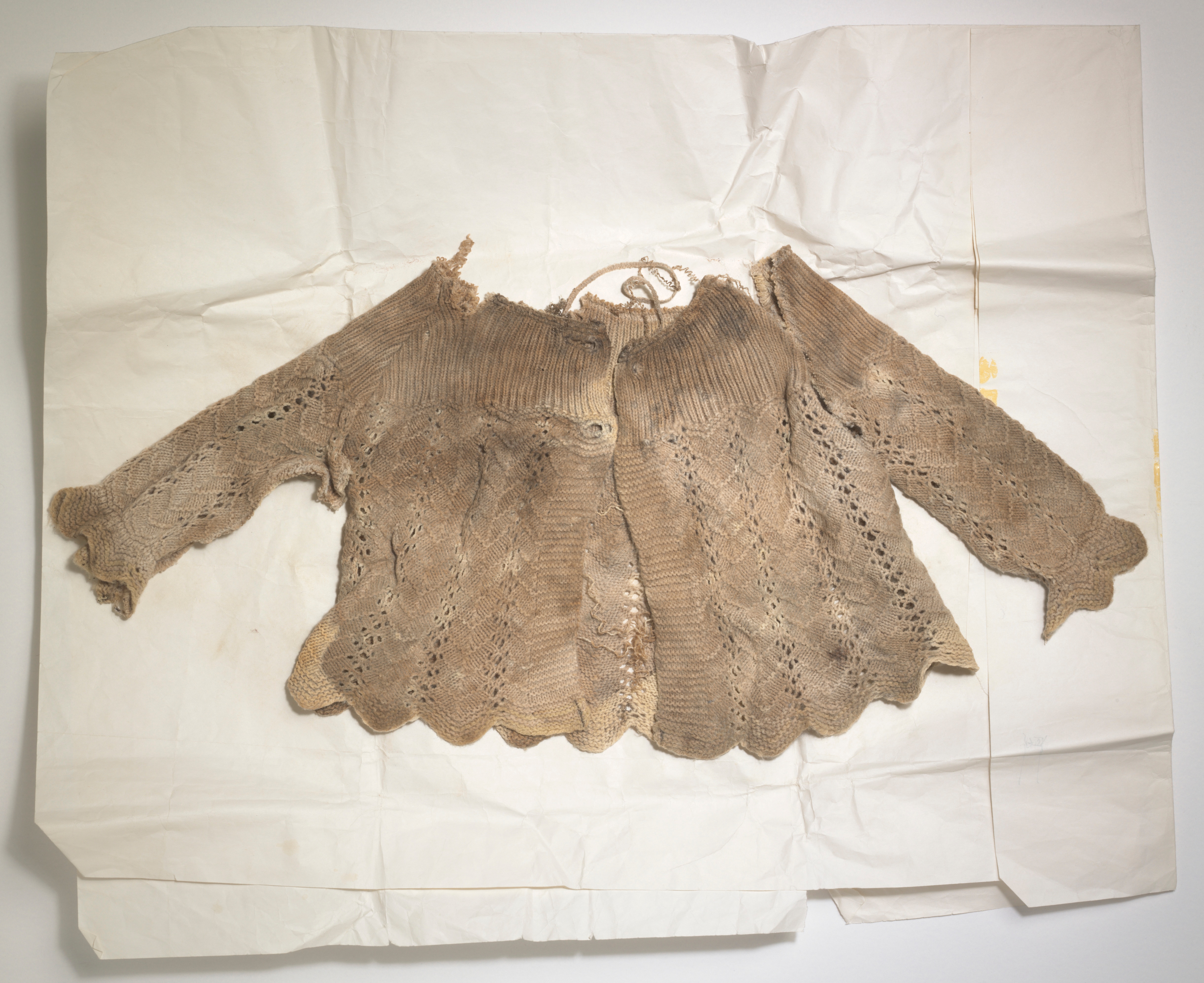 A small, dirty knit jacket laid flat on tissue paper.