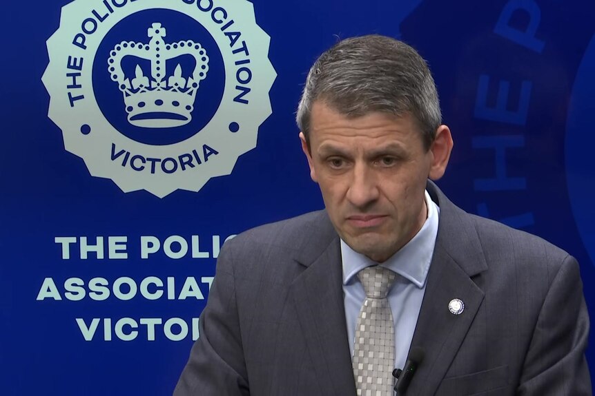 Wayne Gatt stands in front of the Police Association Victoria logo and stares, with his eyes cast downwards.