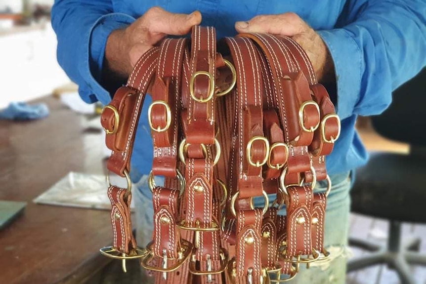 A man holds leather knife belts with buckles.