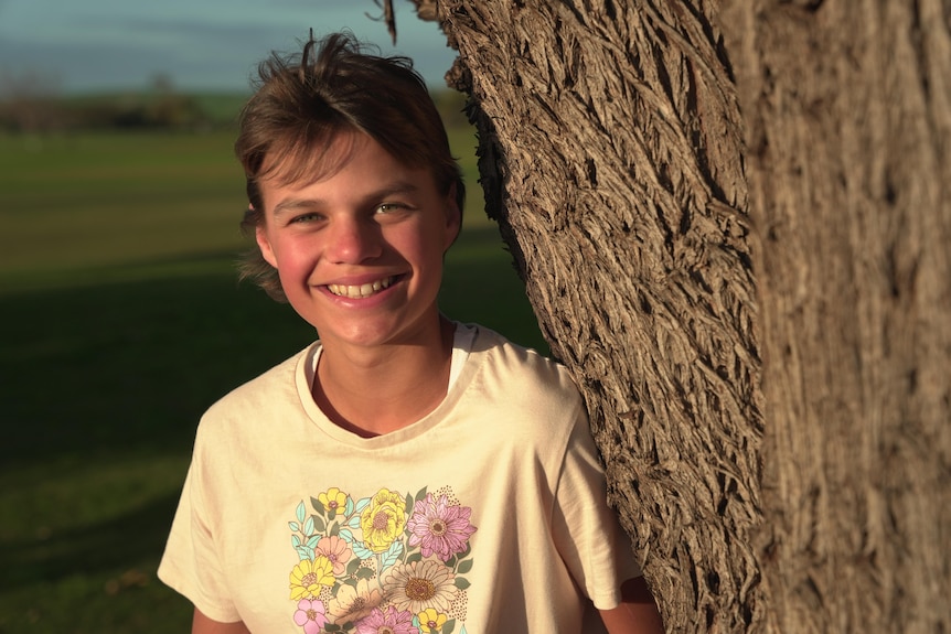 Young girl next to a tree smiling.