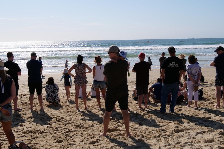 A crowd spaced evenly on a beach looking at the sun hitting the water.